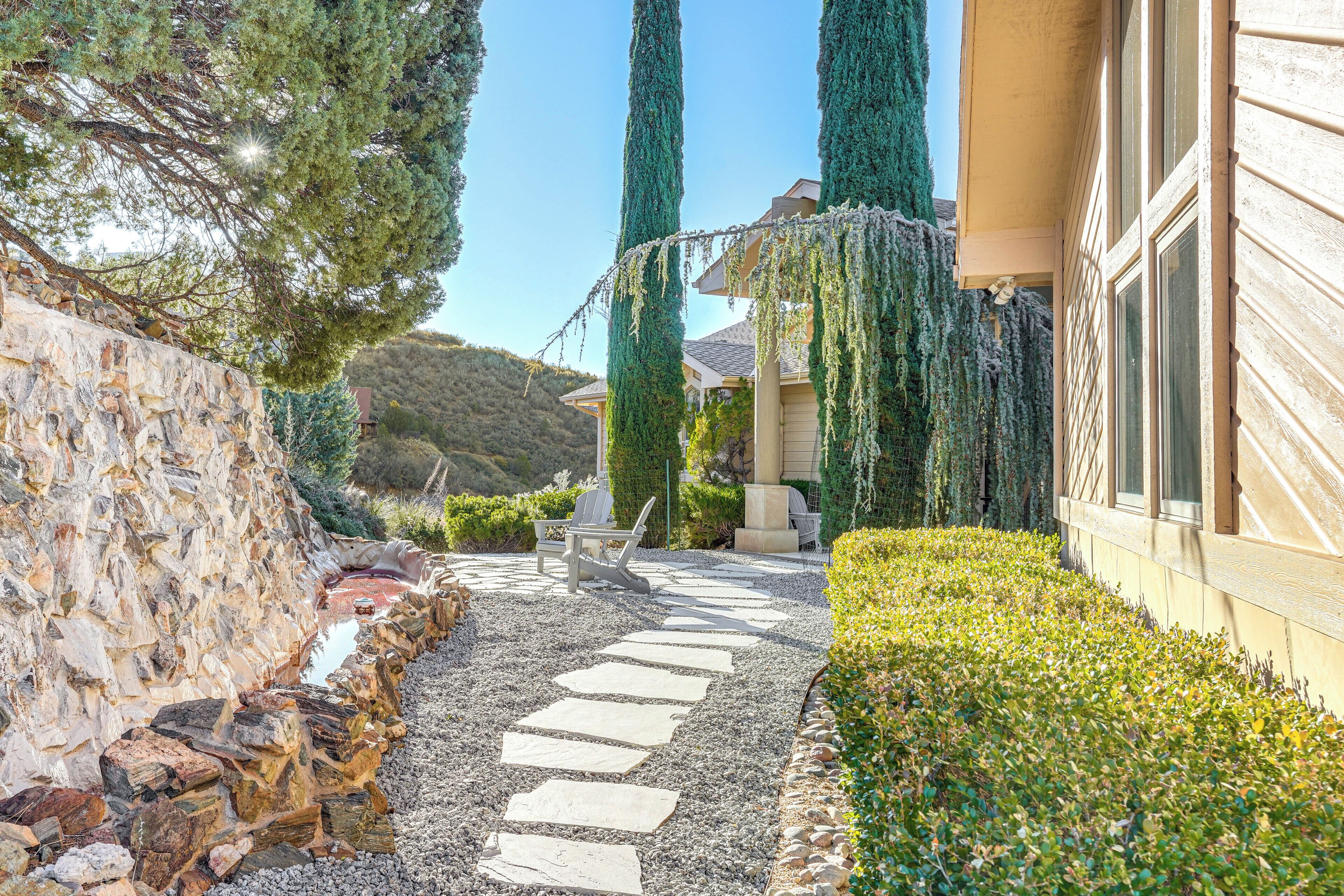 Ein Steinweg führt zu einem Haus mit einer Steinmauer und einem Garten mit Stuhl und Tisch.