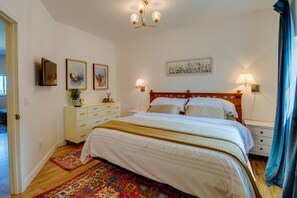 A bedroom with a wooden bed, white bedding, a patterned rug, a nightstand, a wall-mounted lamp, and artwork. - Port Angeles Apartment Near Olympic Natl Park! (Port Angeles)