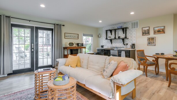 A living room with a sofa, a dining table, chairs, a kitchen area, and a view through large windows.
