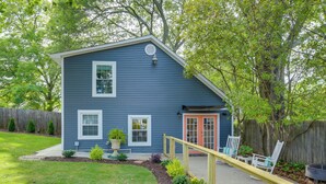 A blue house with a wooden deck, a red door, and a fenced backyard with a small garden.