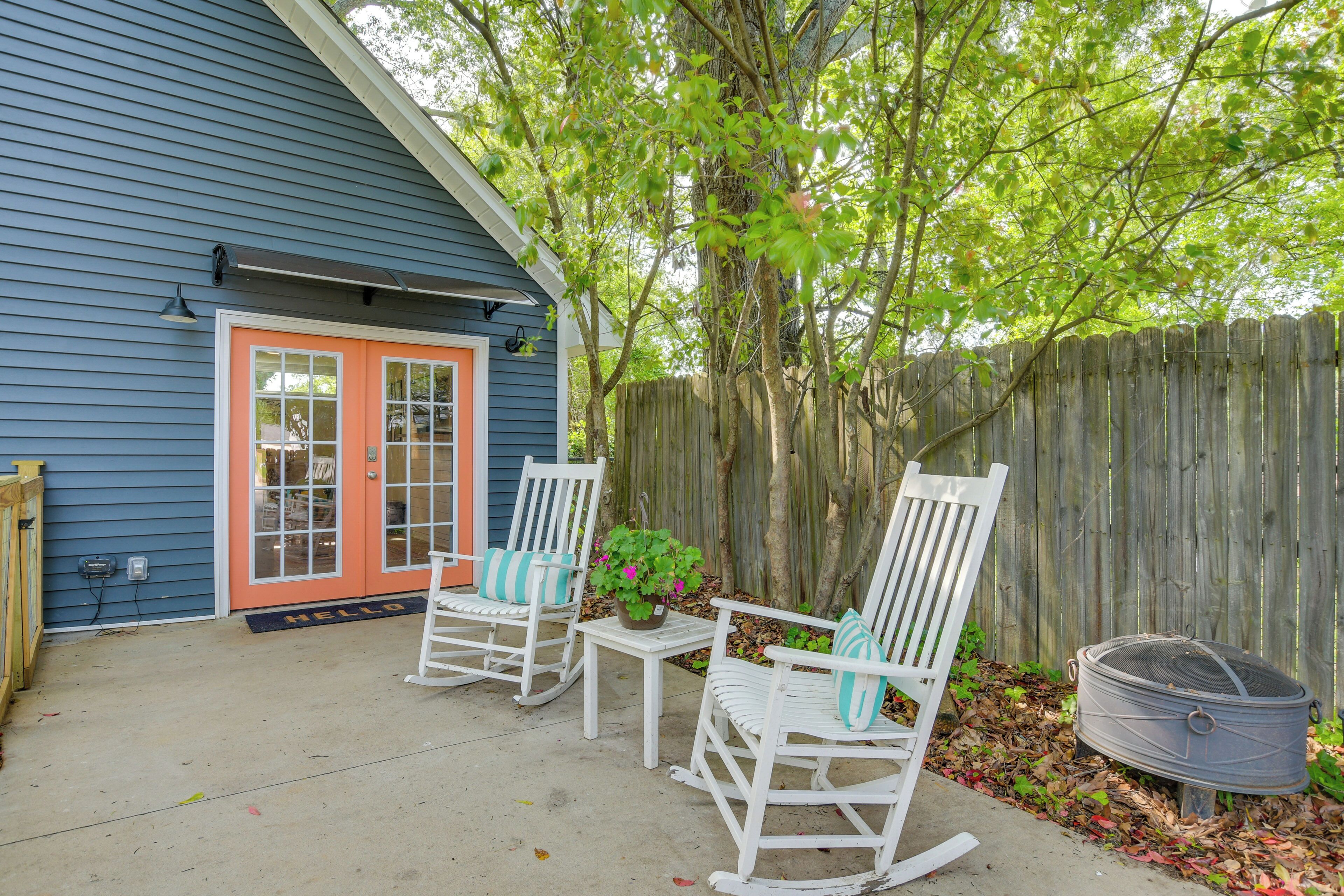 A blue house with a red door, two rocking chairs, a small table, and a fire pit.