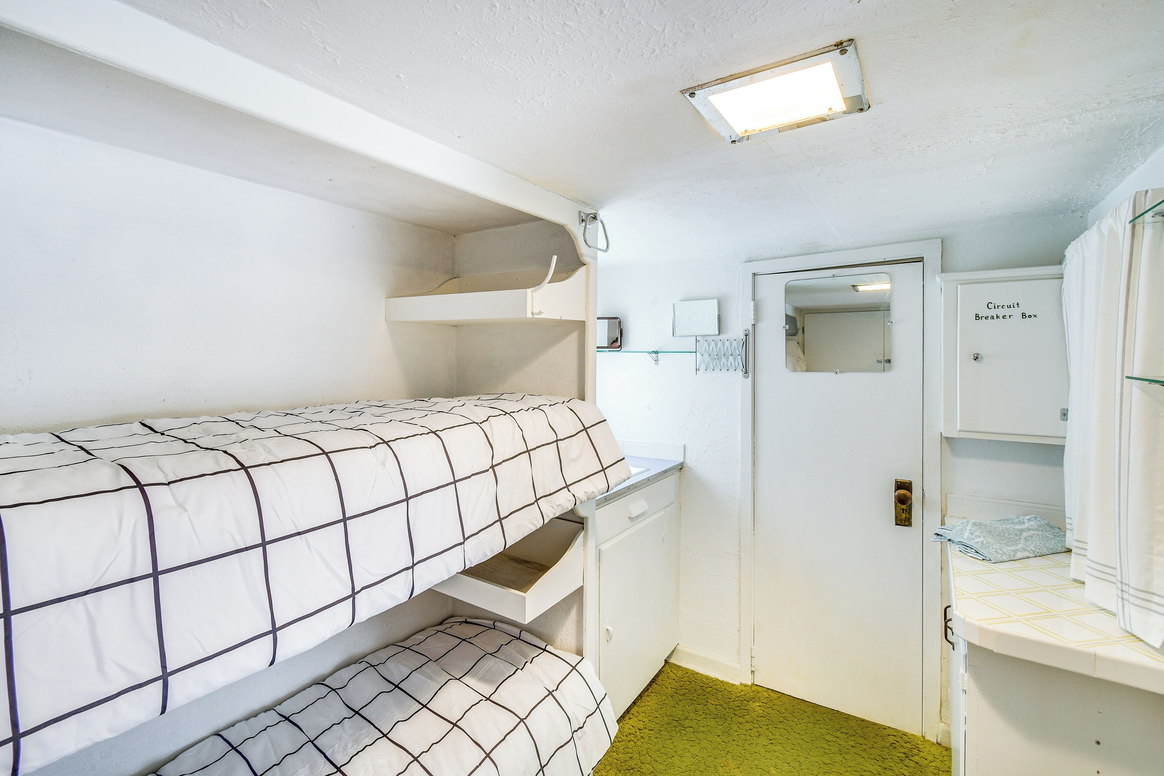 A bunk bed with a white and black checkered bedspread, a white dresser with a mirror, and a door labeled "Circuit Breaker Box".