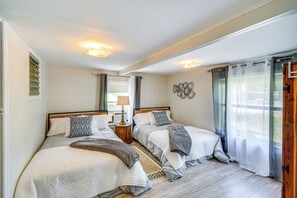 Un dormitorio con dos camas, una mesita de noche, una lámpara y una ventana con cortinas.