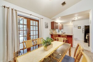 A dining area with a glass table, wicker chairs, and a central potted plant.