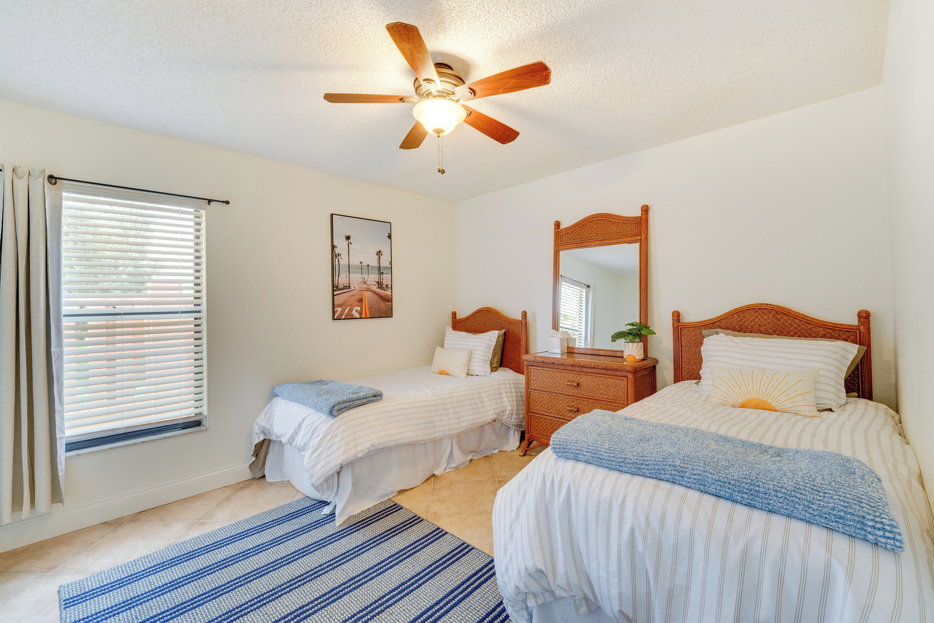 A bedroom with two beds, a ceiling fan, a wooden dresser, and a window with blinds.