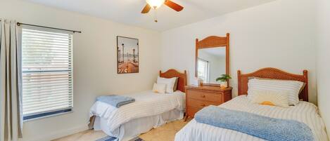 A bedroom with two beds, a ceiling fan, a wooden dresser, and a window with blinds.
