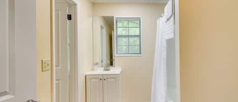 A narrow hallway with a white door, a white vanity with a mirror, and a window with blinds.