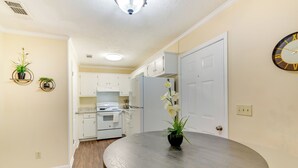 Una cocina moderna con armarios blancos, un refrigerador blanco y una mesa de comedor de madera con una orquídea en maceta.