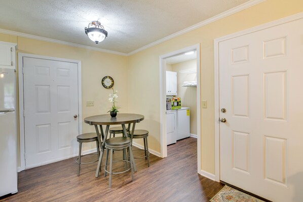 A dining area with a round table and four stools, a ceiling light fixture, and a door leading to a kitchen.