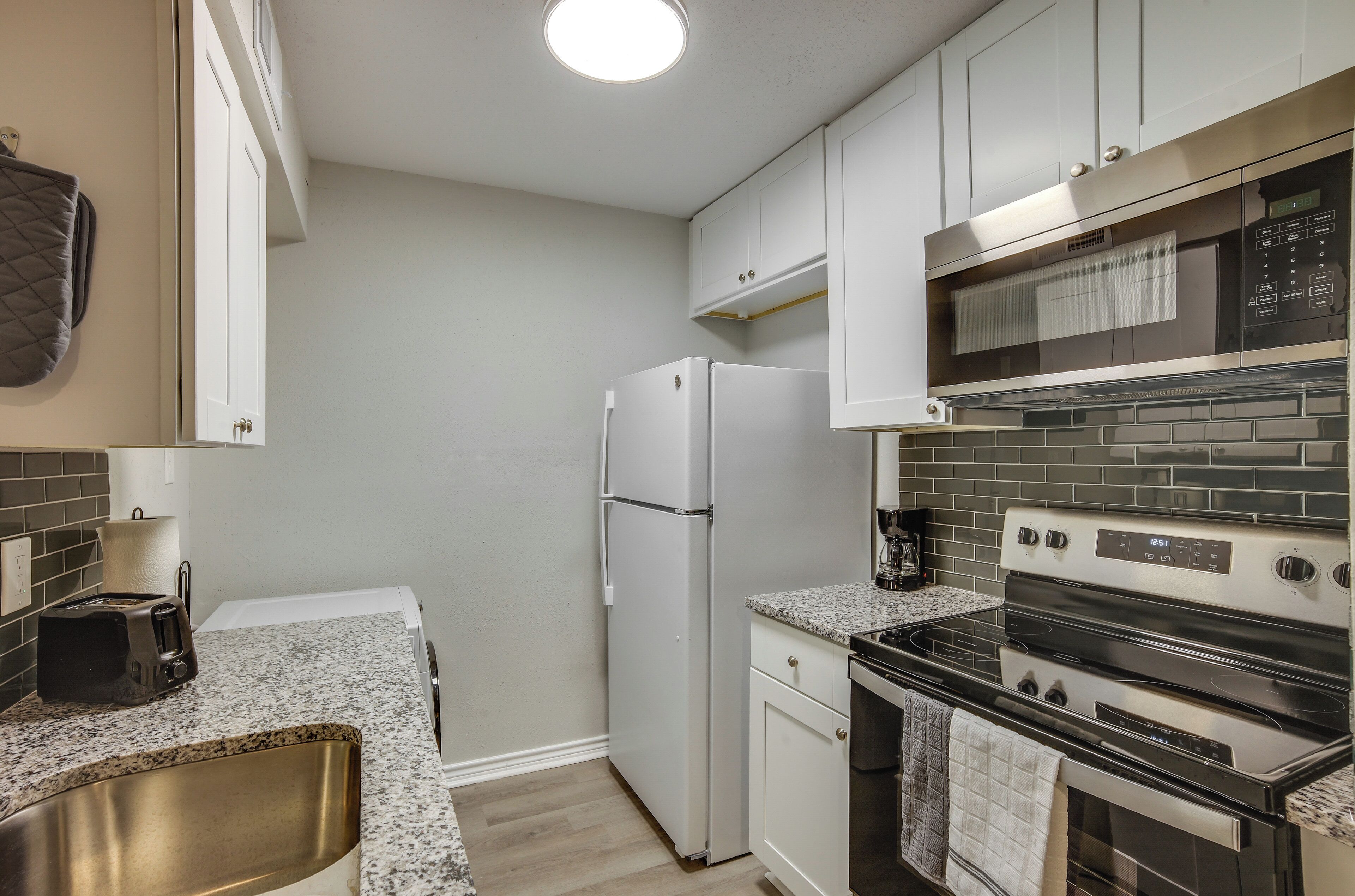 A compact kitchen with white cabinets, a stainless steel oven, a microwave, and a refrigerator.