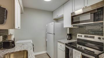A compact kitchen with white cabinets, a stainless steel oven, a microwave, and a refrigerator.