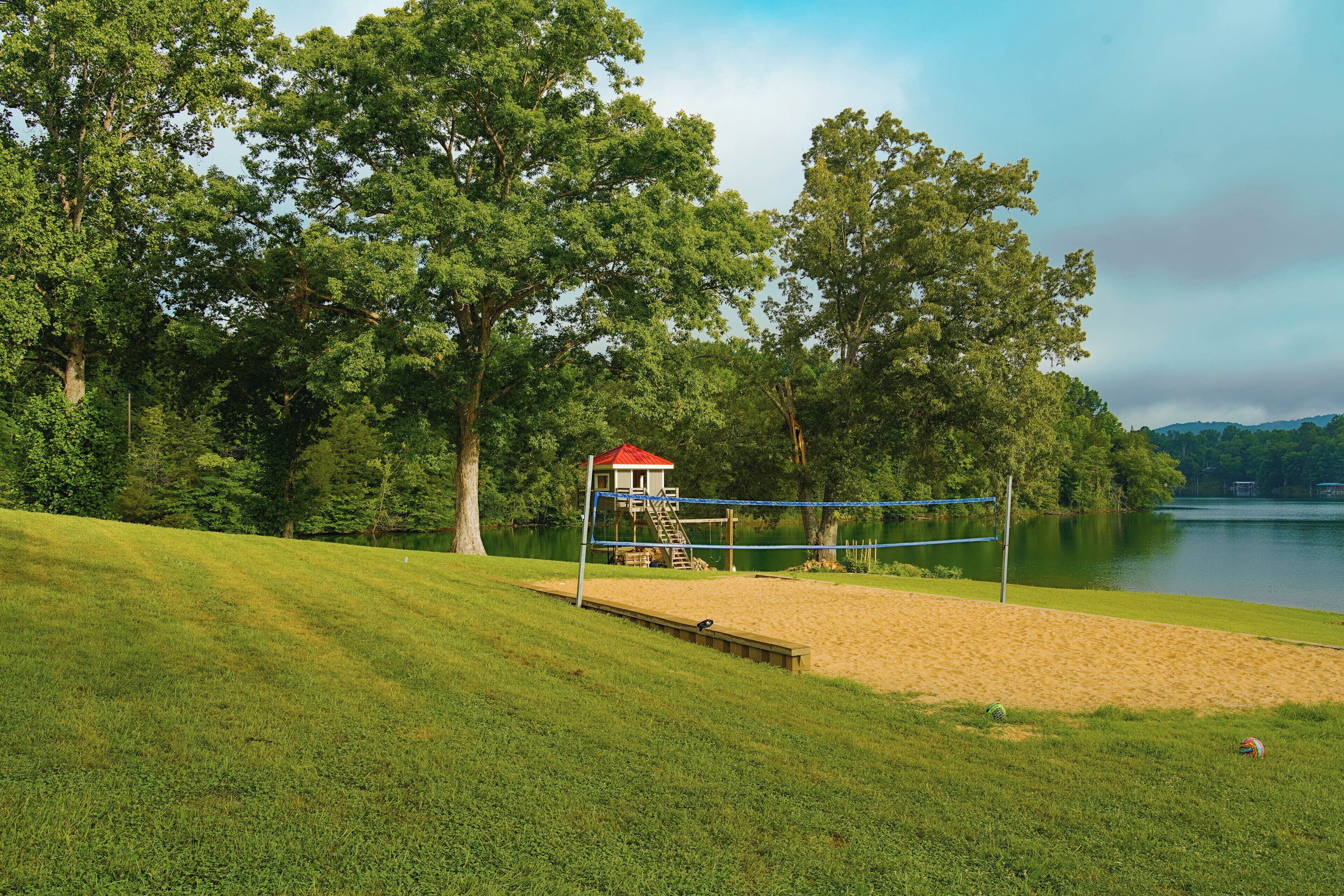 A beach volleyball court with a lifeguard tower, surrounded by trees and a lake.
