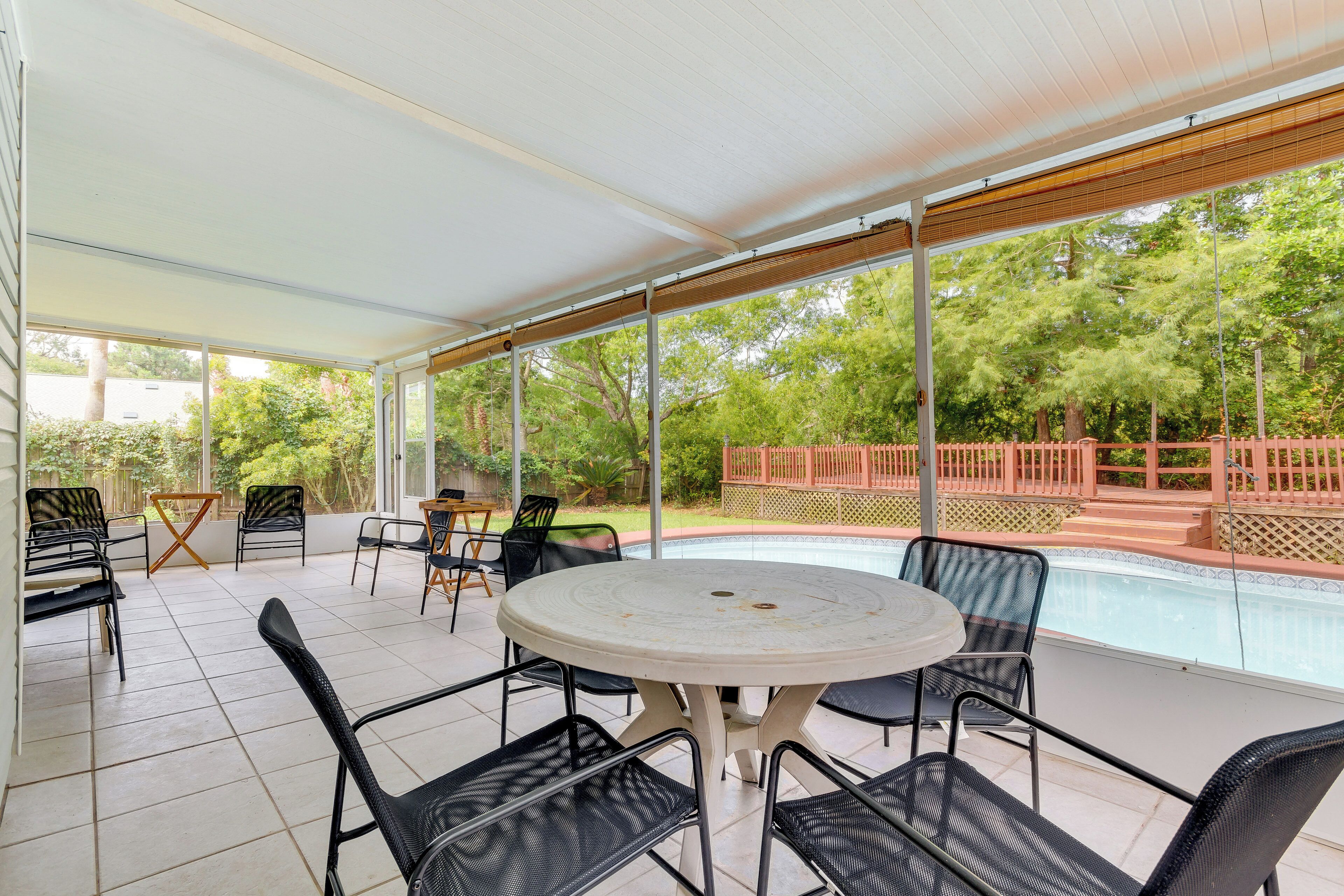 A covered patio with a pool, outdoor seating, and a view of the surrounding greenery.