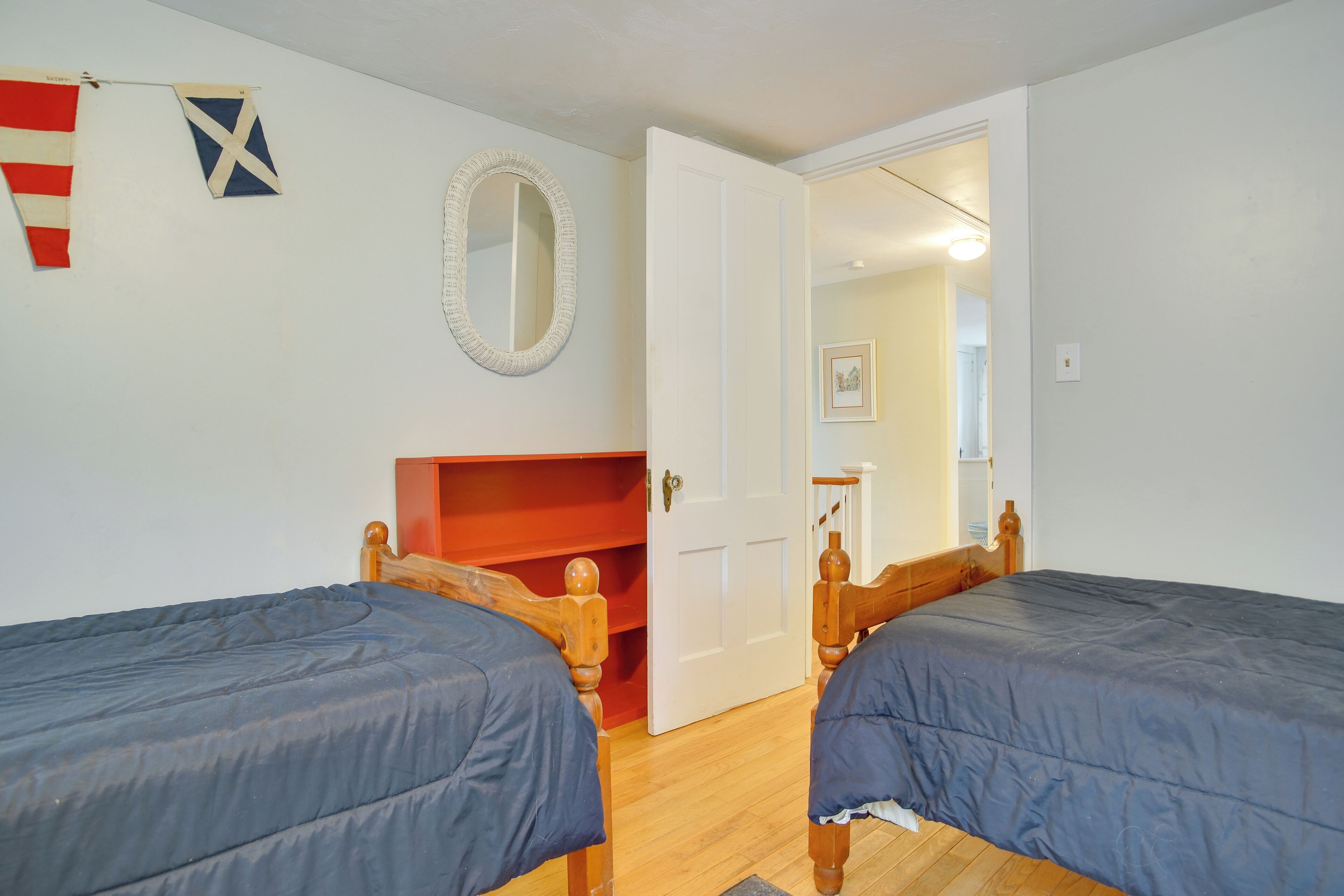 A room with two wooden beds, a red shelf, a white door, and a mirror on the wall.
