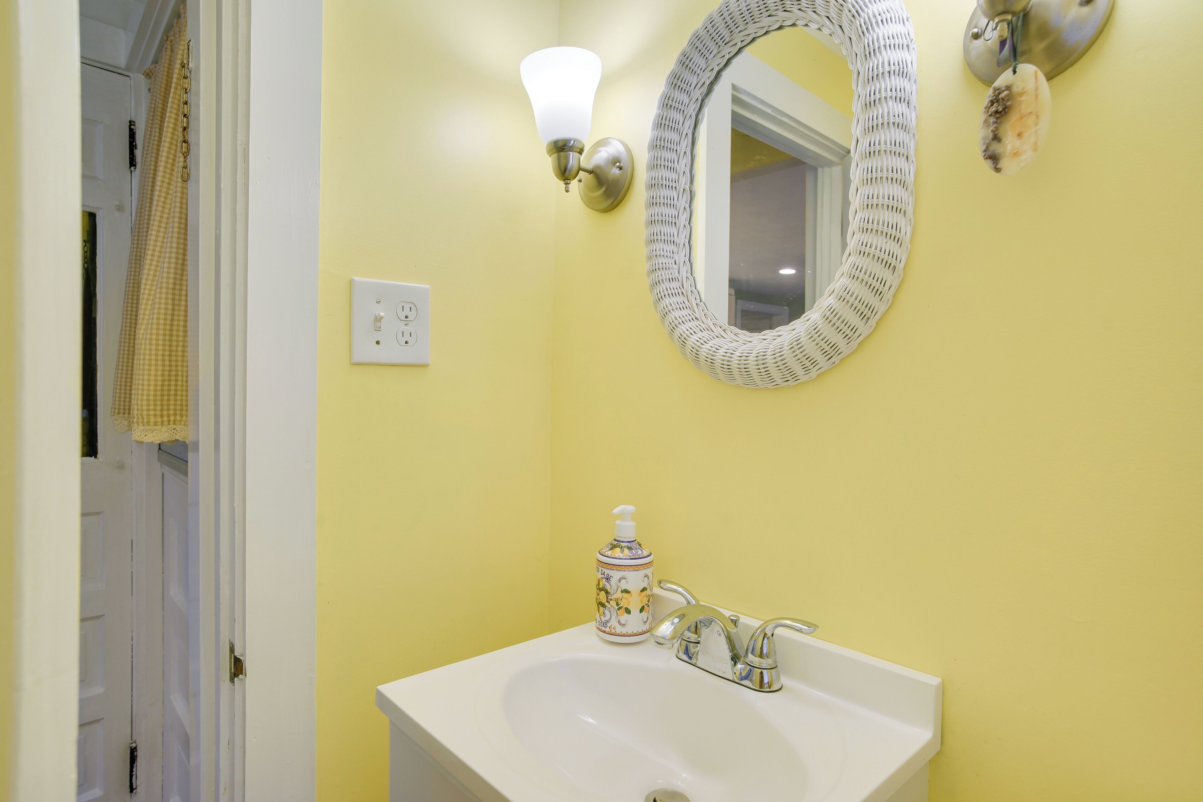 A bathroom with a white sink, a mirror, and a wall-mounted light fixture.
