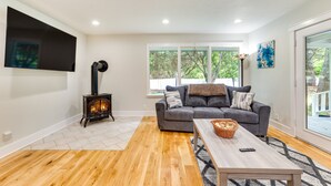 Un salon avec une cheminée, un canapé gris, un plancher en bois et une grande fenêtre.