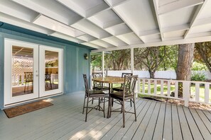 Un patio techado con una mesa y sillas, una cerca blanca y árboles al fondo.