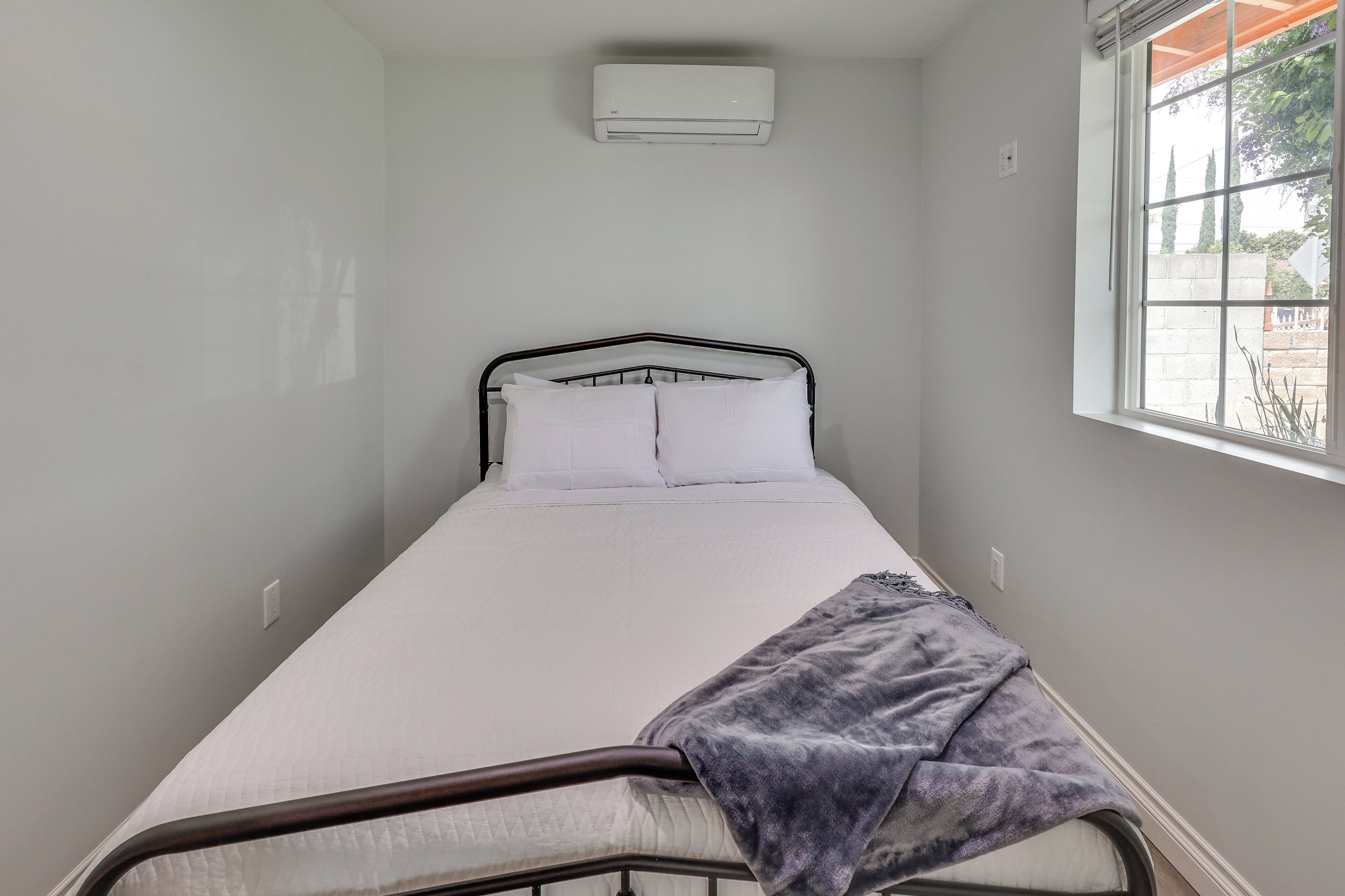 Ein Einzelbett mit Metallgestell, weißer Bettwäsche und einer grauen Decke.