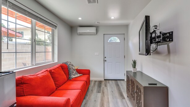 A hallway with a red sofa, a white door, and a wall-mounted TV. - Sleek San Fernando Studio ~ 14 Mi to Universal (San Fernando)