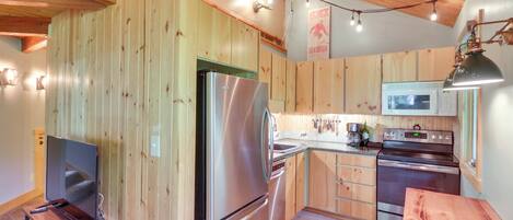 A kitchen with wooden walls, stainless steel appliances, a wooden table, and a TV.