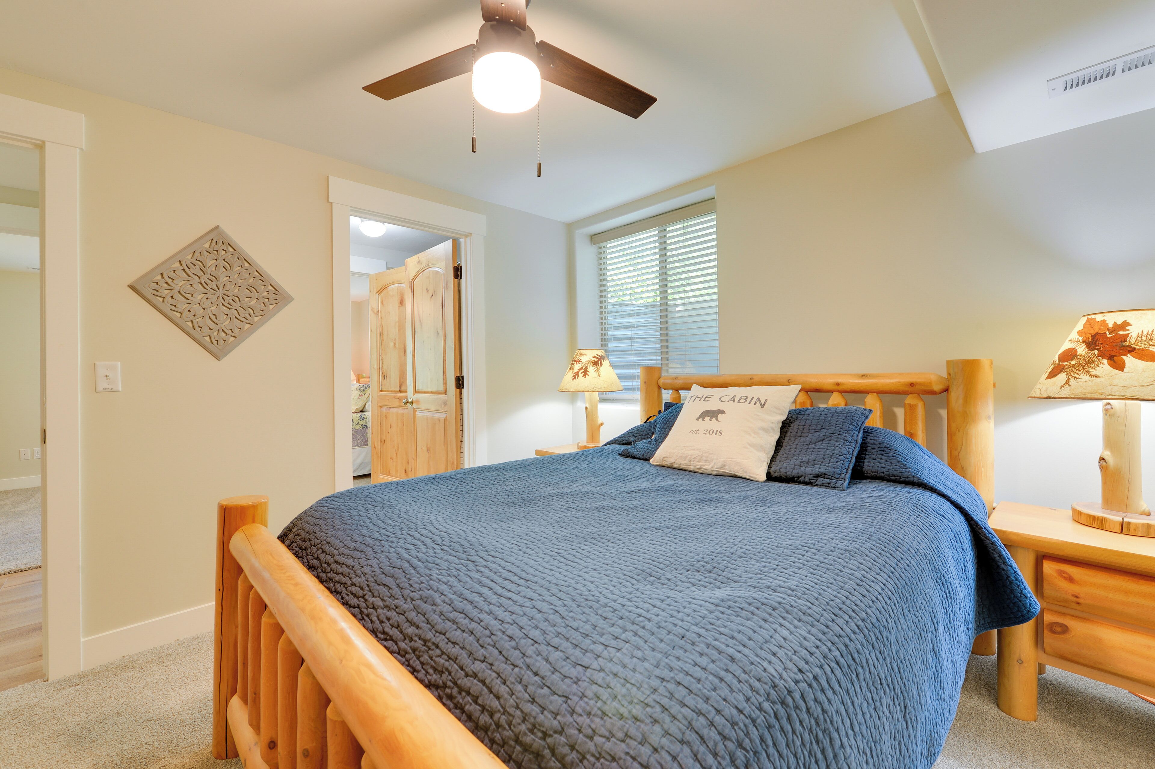 A bedroom with a wooden bed, a ceiling fan, a nightstand, a lamp, and a window with blinds.