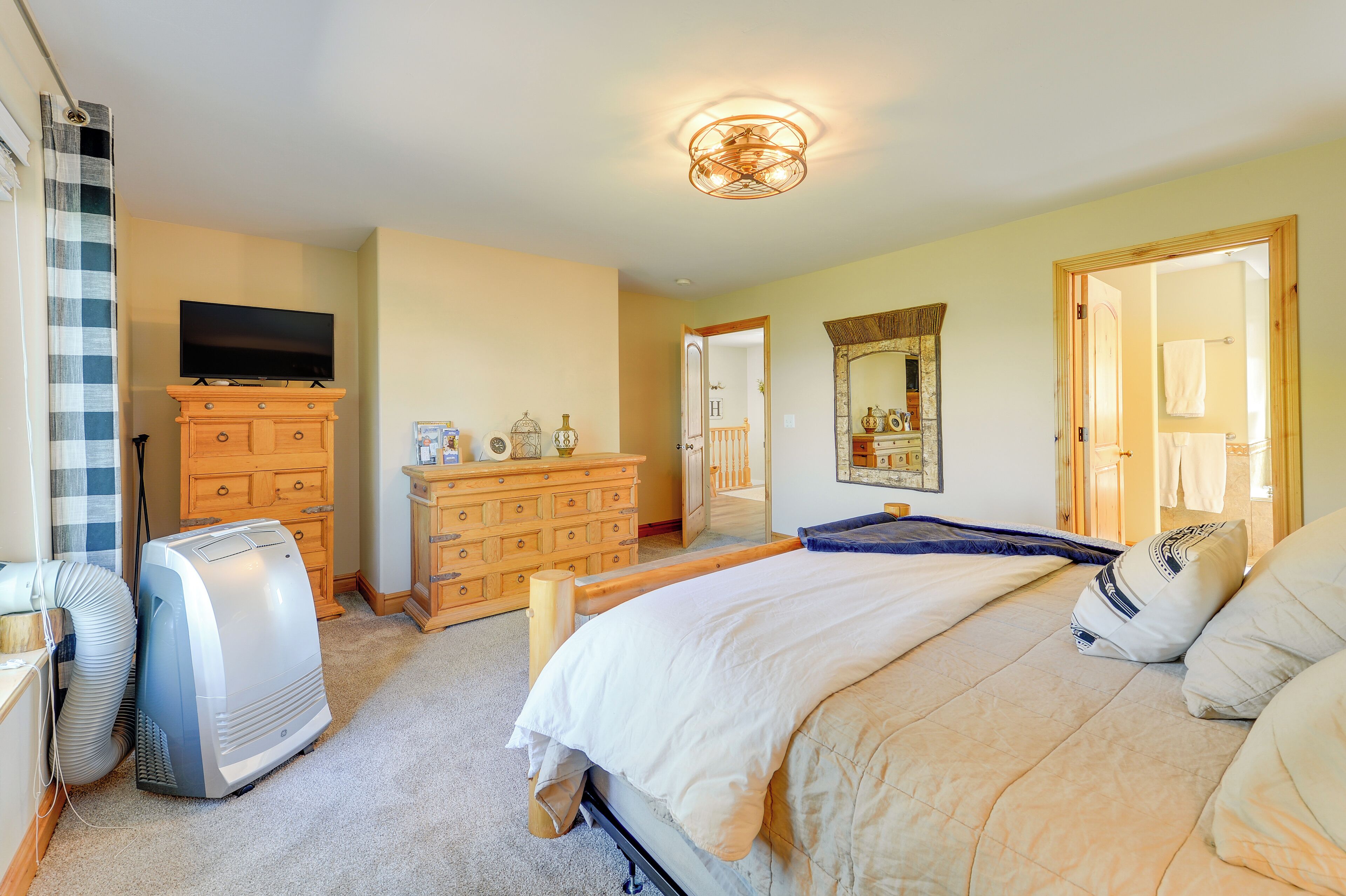 A bedroom with a bed, wooden dresser, television, and a ceiling light fixture.