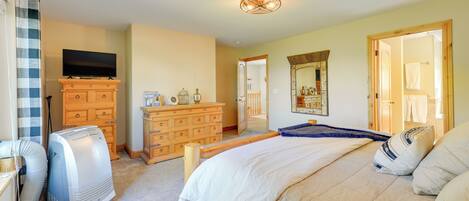 A bedroom with a bed, wooden dresser, television, and a ceiling light fixture.