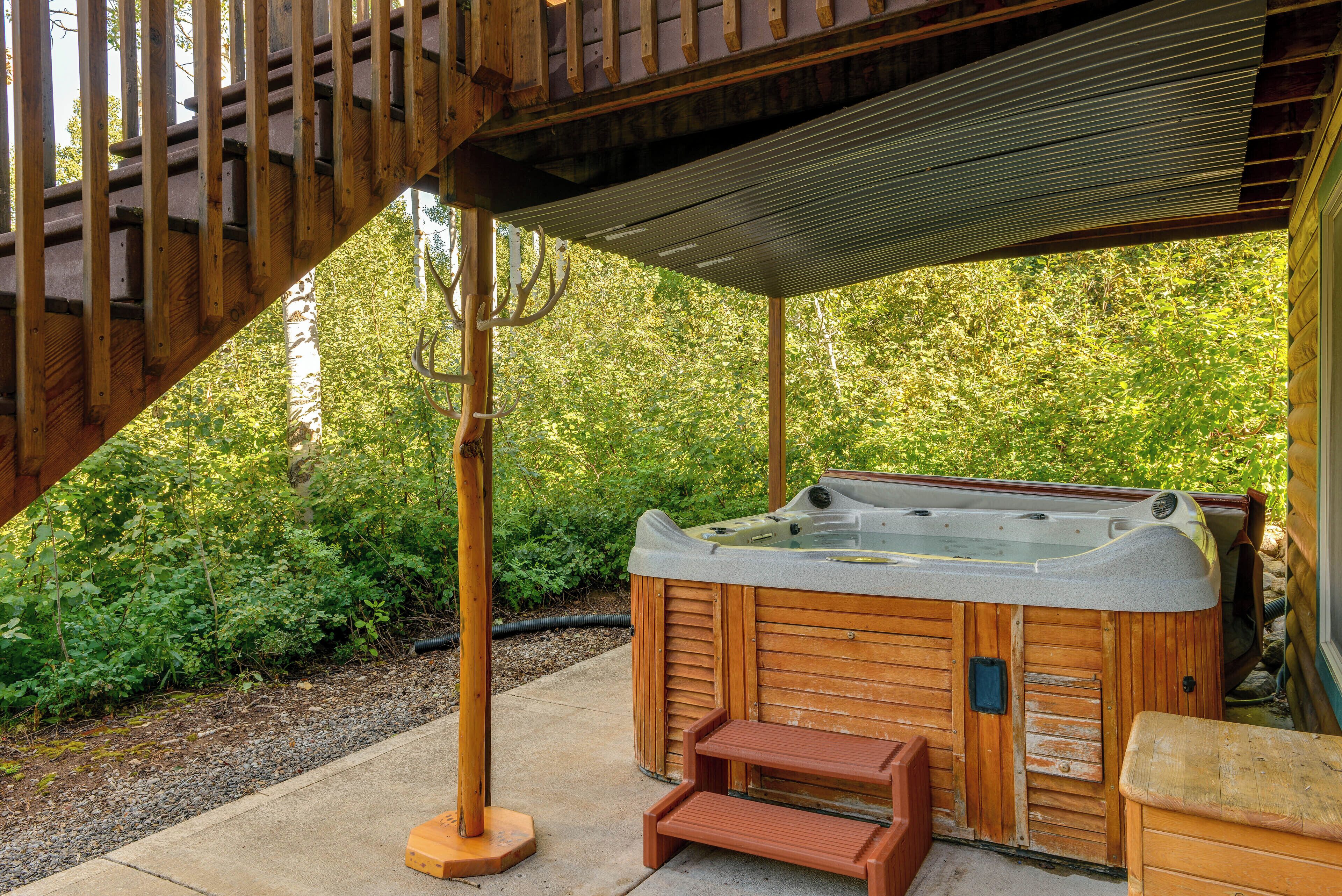 A wooden hot tub under a wooden pergola with steps leading up to it, surrounded by greenery.