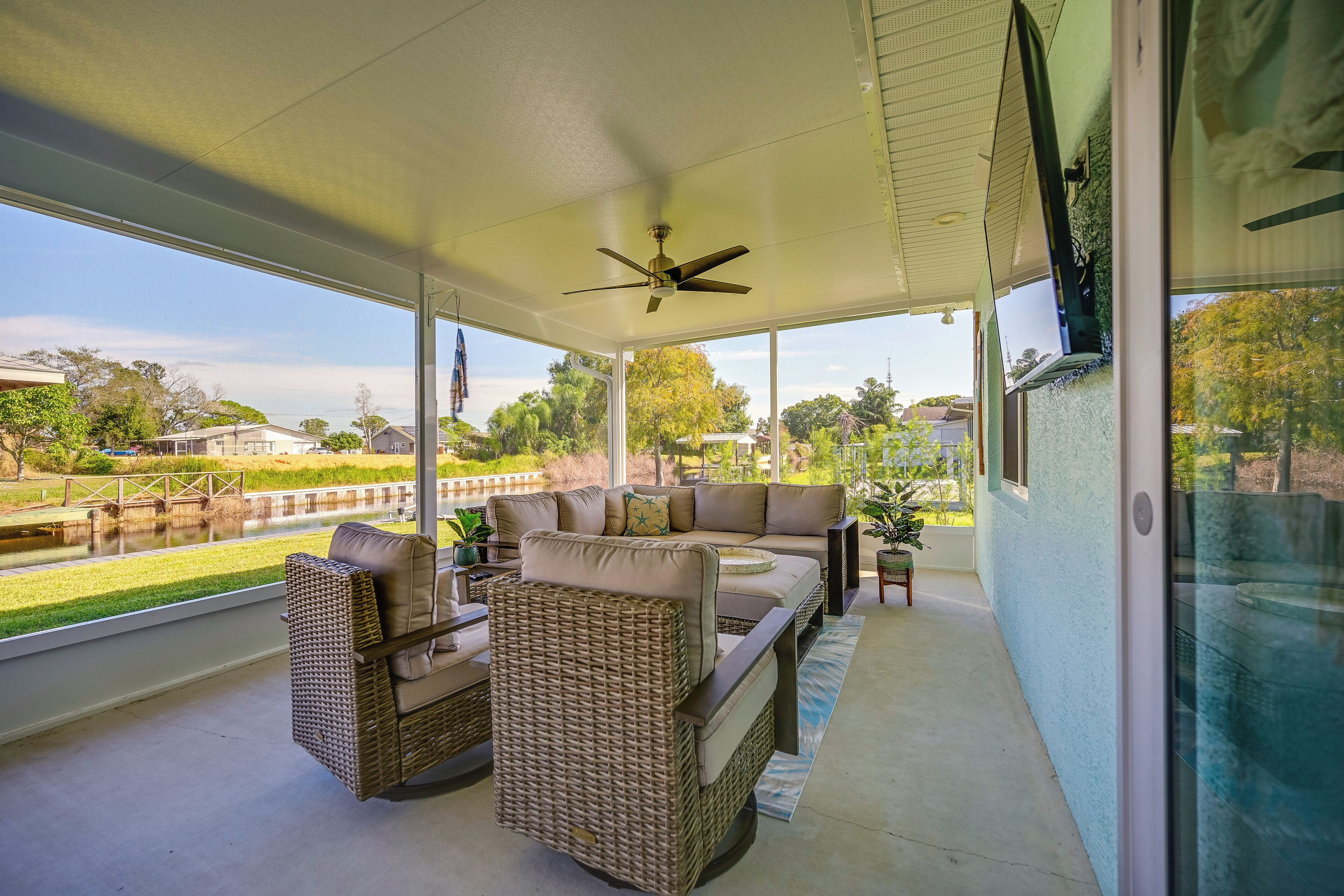 A covered outdoor seating area with wicker furniture, a ceiling fan, and a view of a park and waterway.