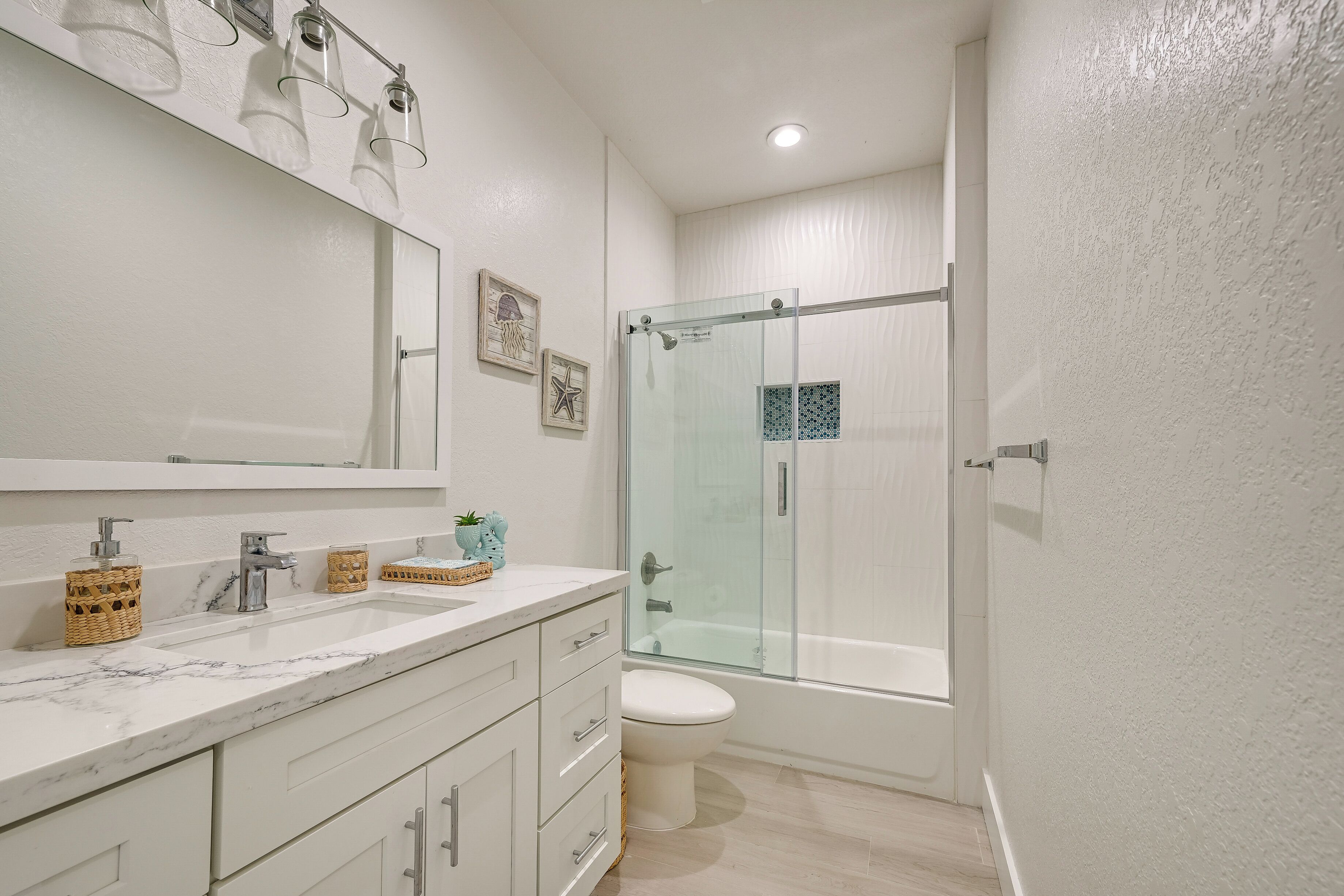 A modern bathroom with a large mirror, white marble countertop, and a glass-enclosed shower.