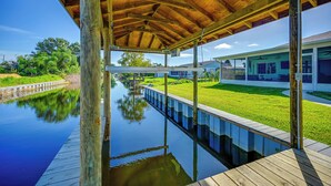 A covered wooden deck with a view of a calm water body and a grassy area with a building in the background. - Sebring Serenity: Waterfront Retreat w/ Boat Dock! (Sebring)