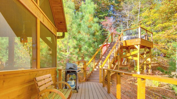 A wooden deck with a bench and a wheelbarrow, leading to a wooden staircase and lookout platform surrounded by trees. - 7 Mi to Lake Lure: Mill Spring Cabin w/ Hot Tub (Mill Spring)