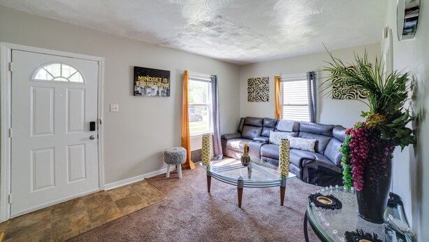 A living room with a glass coffee table, a sofa, a door, and a plant. - Gary Vacation Rental ~ 5 Mi to Lake Michigan! (Gary)