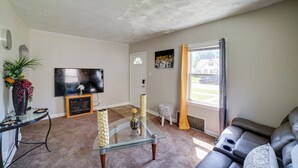 A living room with a glass coffee table, a sofa, a TV, and a fireplace. - Gary Vacation Rental ~ 5 Mi to Lake Michigan! (Gary)