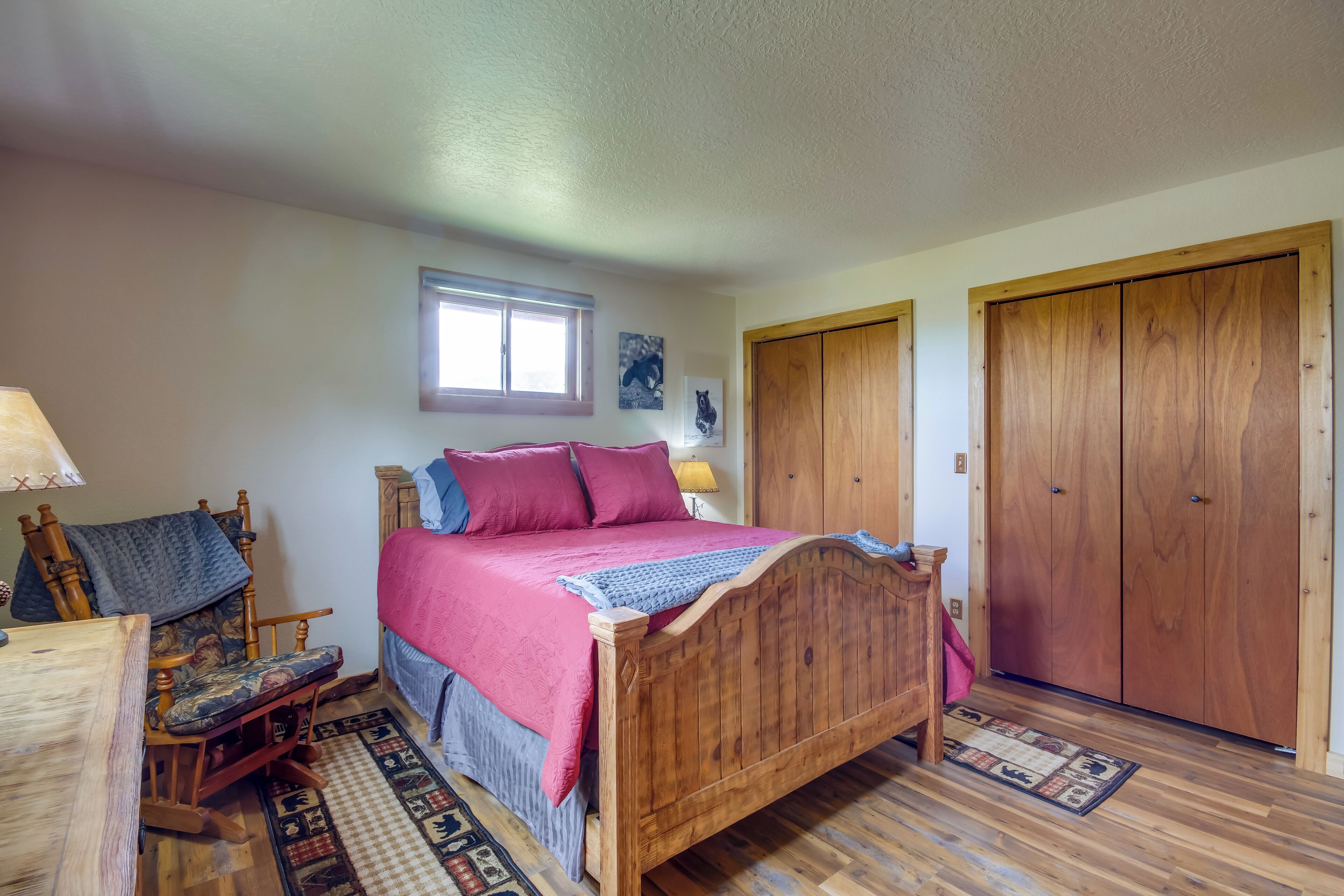 A bedroom with a wooden bed, a chair, a desk, a window, and wooden wardrobes.
