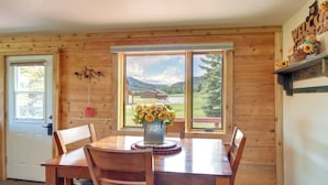 A wooden interior with a dining table set for four, a large window with a view of mountains, and a welcome sign with sunflowers.