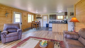 A cozy cabin interior with two leather sofas, a dining area, a kitchen, and a wooden exterior.