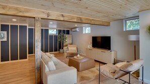 A modern living room with a sofa, coffee table, and a TV. There is a wooden ceiling and a window. - Hot Tub, Fire Pit: Pet-friendly Freehold Home! (Freehold)