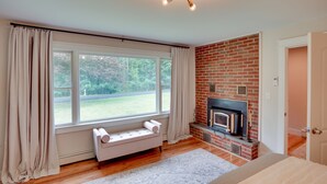 A modern living room with a fireplace, large windows, and a cozy seating area. - Hot Tub, Fire Pit: Pet-friendly Freehold Home! (Freehold)