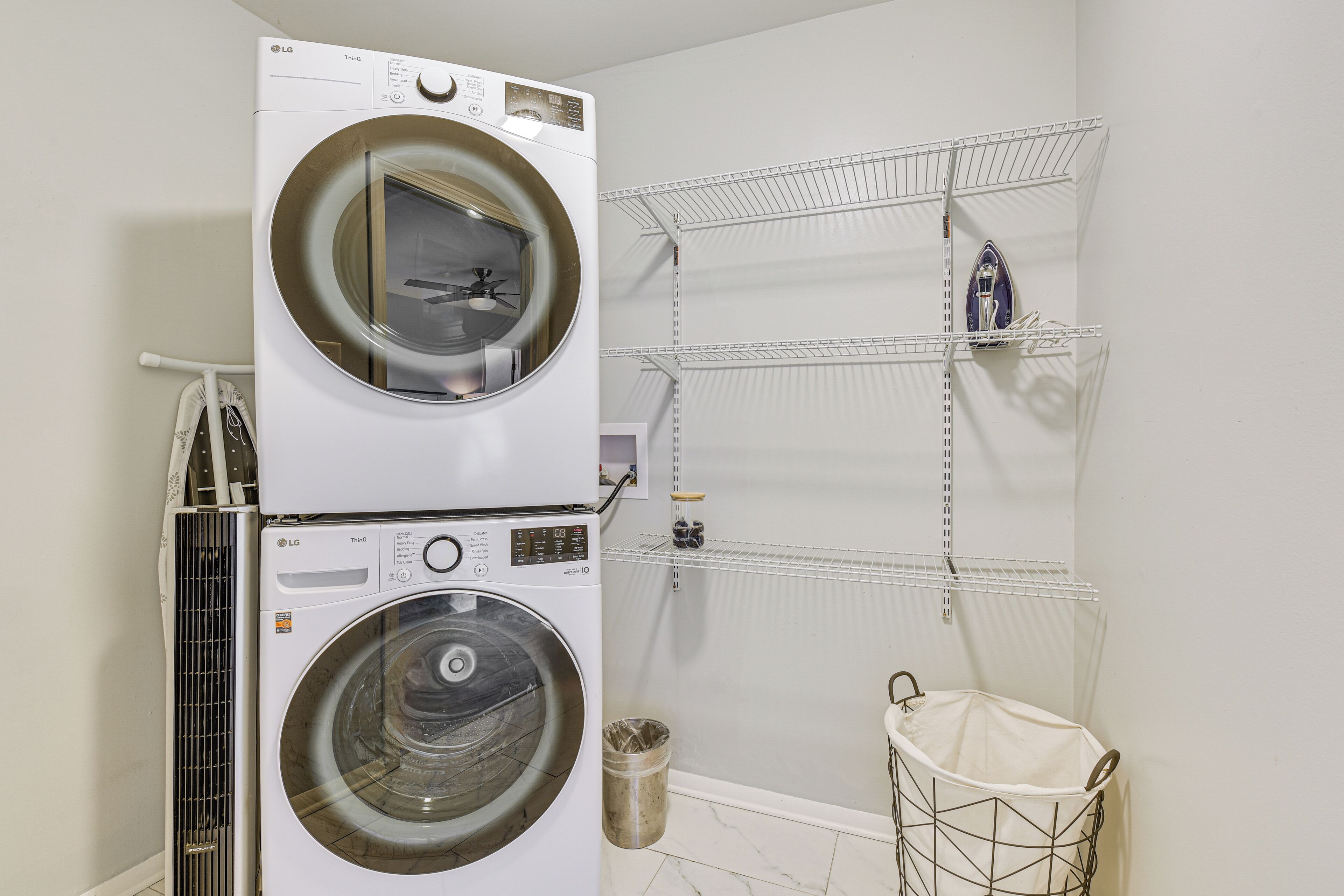 A laundry room with stacked washers and dryers, metal shelving, and a trash can.