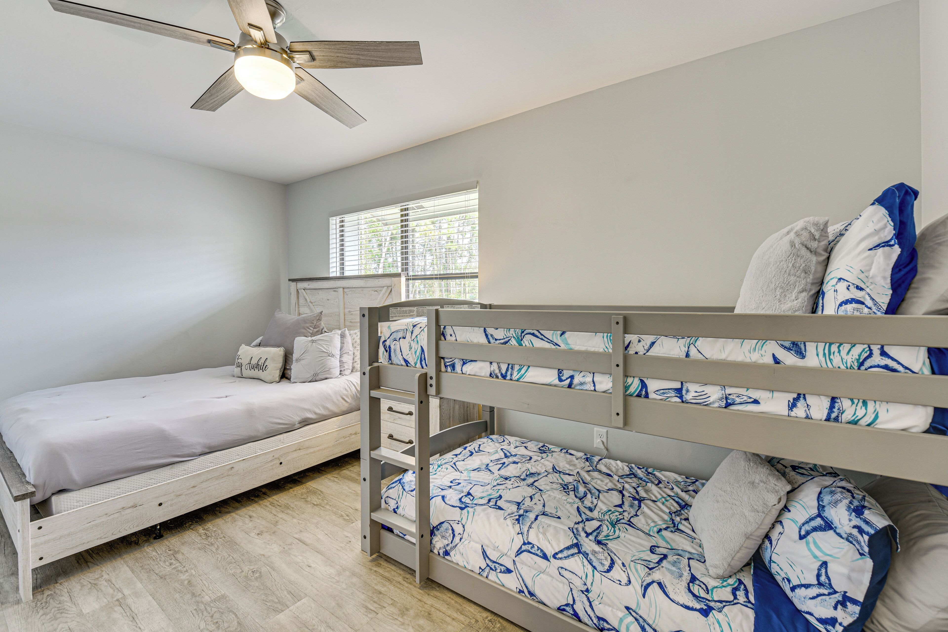 A bedroom with two bunk beds, a ceiling fan, a window with blinds, and a bedside table.