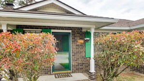 A house with a brick exterior, a green door, and a porch with a basket and hanging planter.