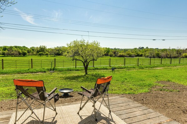 A wooden deck with two camping chairs facing a grassy field with a fence and trees. - Family-friendly Lander Home Rental: Yard, Patio! (Lander)