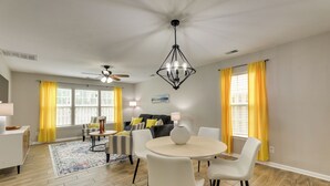 A dining area with a round table and chairs, a ceiling fan, and a chandelier.