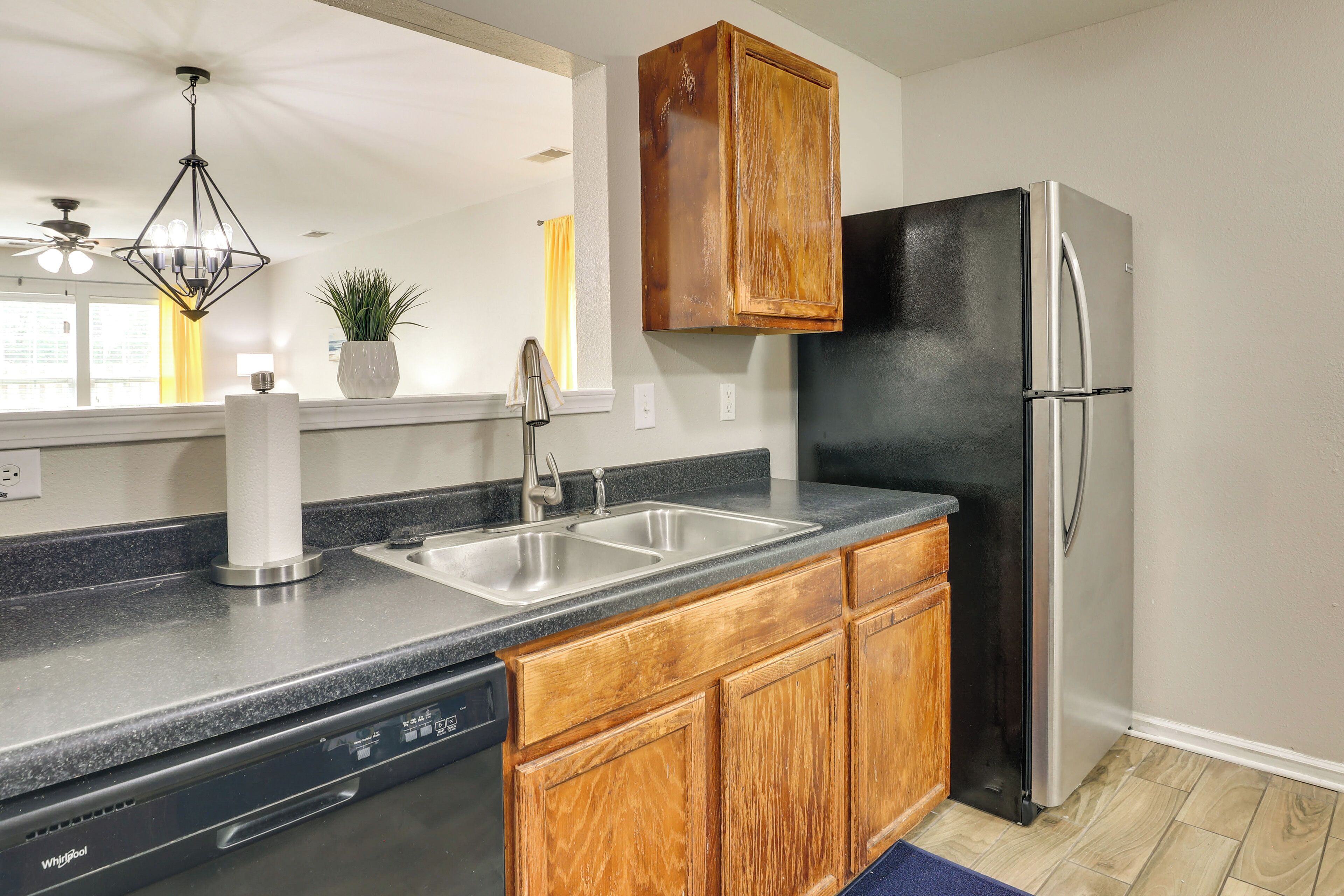A kitchen with a dishwasher, double sink, wooden cabinets, and a black refrigerator.