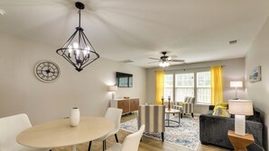 A modern living room with a dining area, a ceiling fan, and a large window with yellow curtains.
