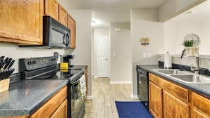 A kitchen with wooden cabinets, a black stove, and a stainless steel sink.