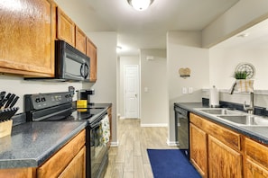 A kitchen with wooden cabinets, a black stove, a microwave, and a sink.