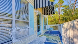 Varanda com um banco de metal branco, um toldo listrado e um chão de madeira azul.