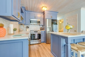 A modern kitchen with blue cabinetry, stainless steel appliances, and a wooden floor.